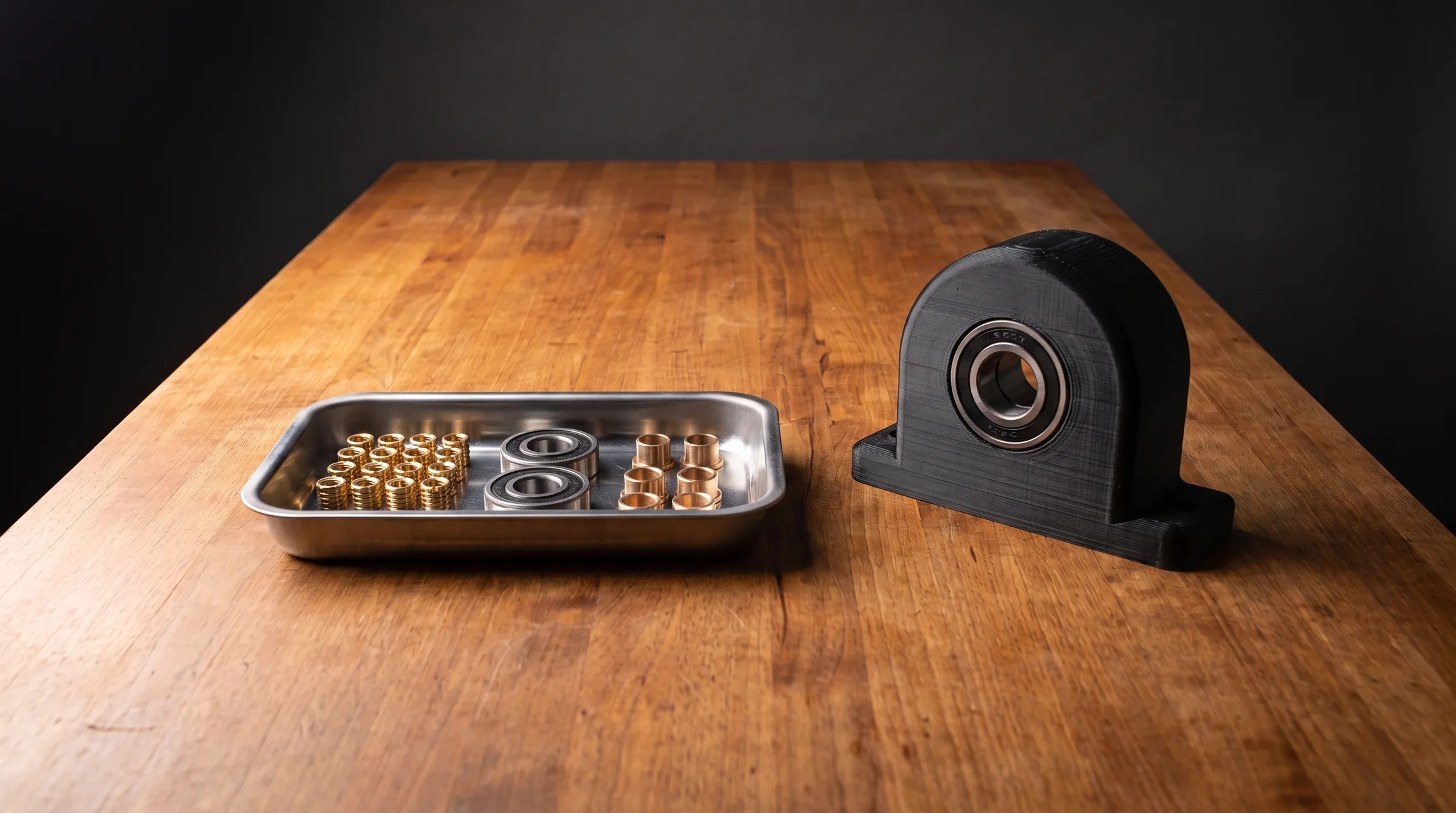 Tray of brass heat-set inserts, bearings, and bushings beside an assembled printed part